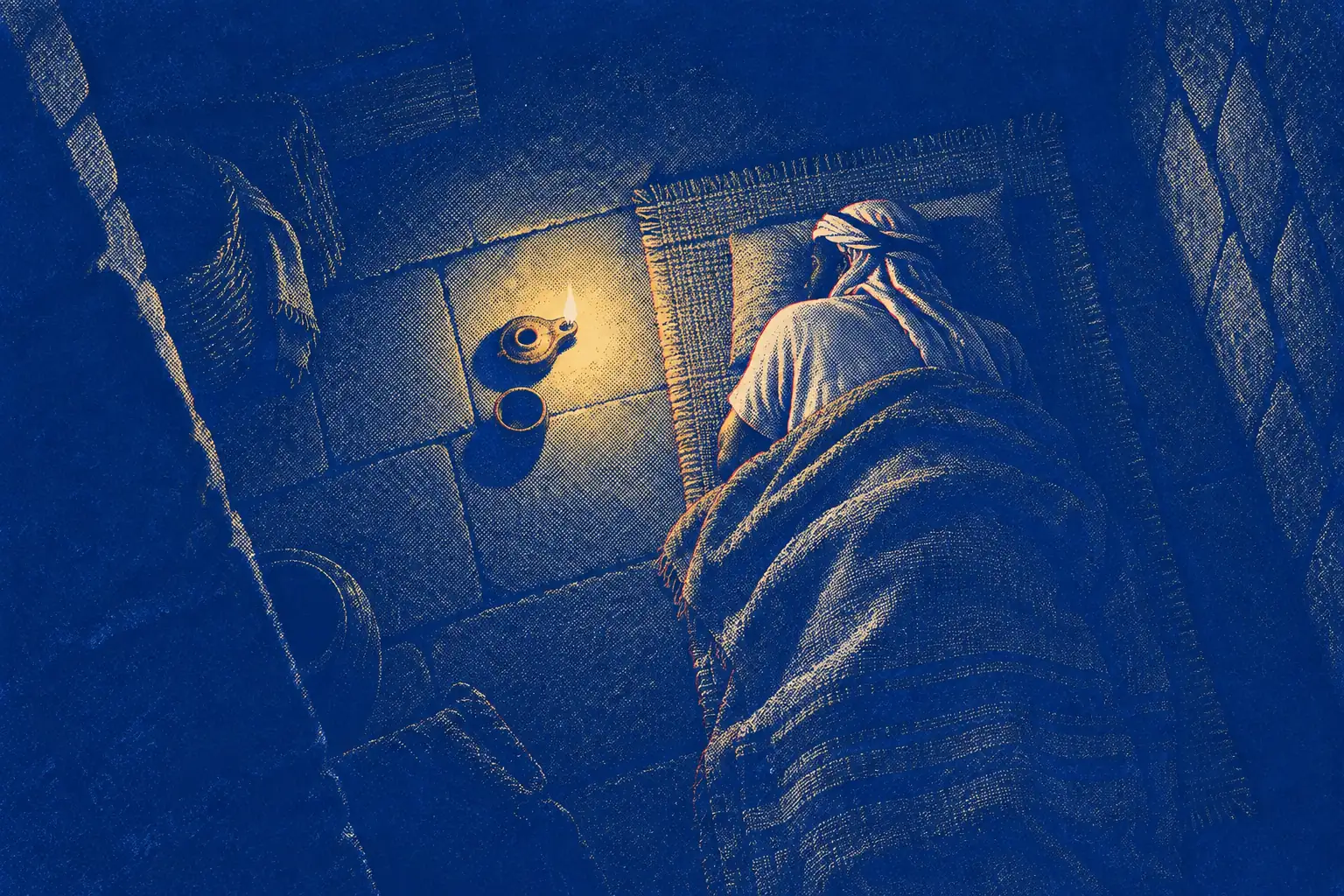 Seen from above in a dark stone room at night, a man lies on a simple woven mat under a rough blanket, turned on his side away from us. Beside the mat a small clay lamp burns low, and its gold light makes a small circle on the floor.